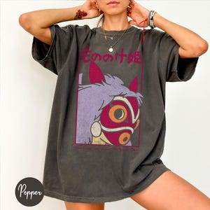 Puede incluir: Camiseta gris oscuro con un dise&ntilde;o de un personaje de una pel&iacute;cula de animaci&oacute;n japonesa. El dise&ntilde;o incluye una m&aacute;scara roja y naranja, cabello morado y texto japon&eacute;s. La camiseta tiene un aspecto vintage.