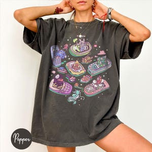 K&ouml;nnte beinhalten: Dunkelgraues T-Shirt mit einem farbenfrohen Grafikdesign von Cartoon-Booten mit Charakteren. Die Boote sind in Gelb-, Rosa-, Blau- und Gr&uuml;nt&ouml;nen gehalten. Das T-Shirt hat eine lockere Passform und kurze &Auml;rmel. Das Wort "Pepper" ist unten links aufgedruckt.