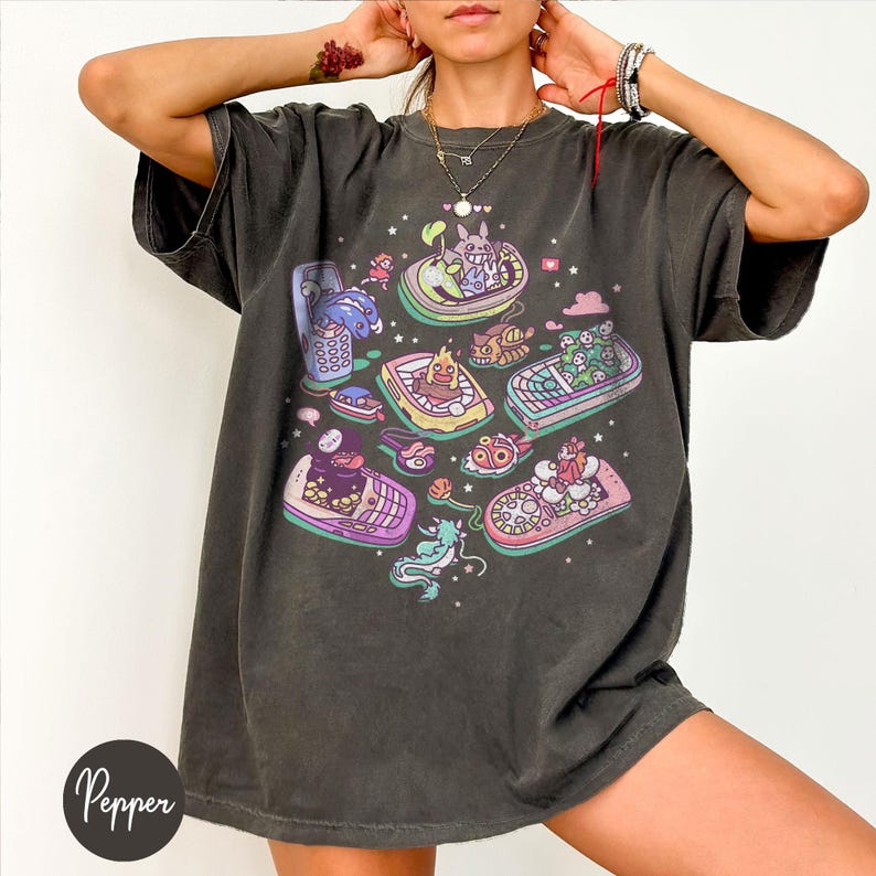 K&ouml;nnte beinhalten: Dunkelgraues T-Shirt mit einem farbenfrohen Grafikdesign von Cartoon-Booten mit Charakteren. Die Boote sind in Gelb-, Rosa-, Blau- und Gr&uuml;nt&ouml;nen gehalten. Das T-Shirt hat eine lockere Passform und kurze &Auml;rmel. Das Wort "Pepper" ist unten links aufgedruckt.