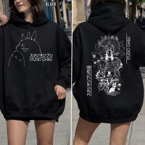 Może przedstawiać: Czarna bluza z kapturem Studio Ghibli z białym konturem Totoro z przodu i szczeg&oacute;łową grafiką z tyłu. Bluza zawiera napis "STUDIO GHIBLI" oraz japoński tekst.