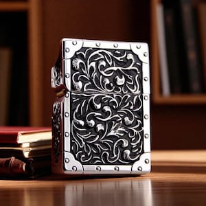 Peut inclure: Un briquet argent&eacute; avec une gravure florale et des volutes complexes. Le briquet est de forme rectangulaire avec des coins arrondis et un couvercle &agrave; charni&egrave;re. Le motif pr&eacute;sente un fond noir avec des d&eacute;tails argent&eacute;s et des rivets.