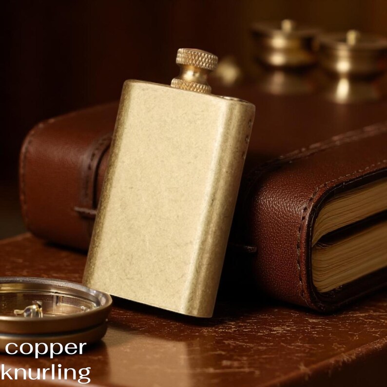 Puede incluir: Una petaca rectangular de color lat&oacute;n con una tapa de rosca texturizada. La petaca se encuentra sobre un fondo borroso con un cuaderno encuadernado en cuero y una br&uacute;jula. Las palabras "copper knurling" est&aacute;n en la parte inferior.