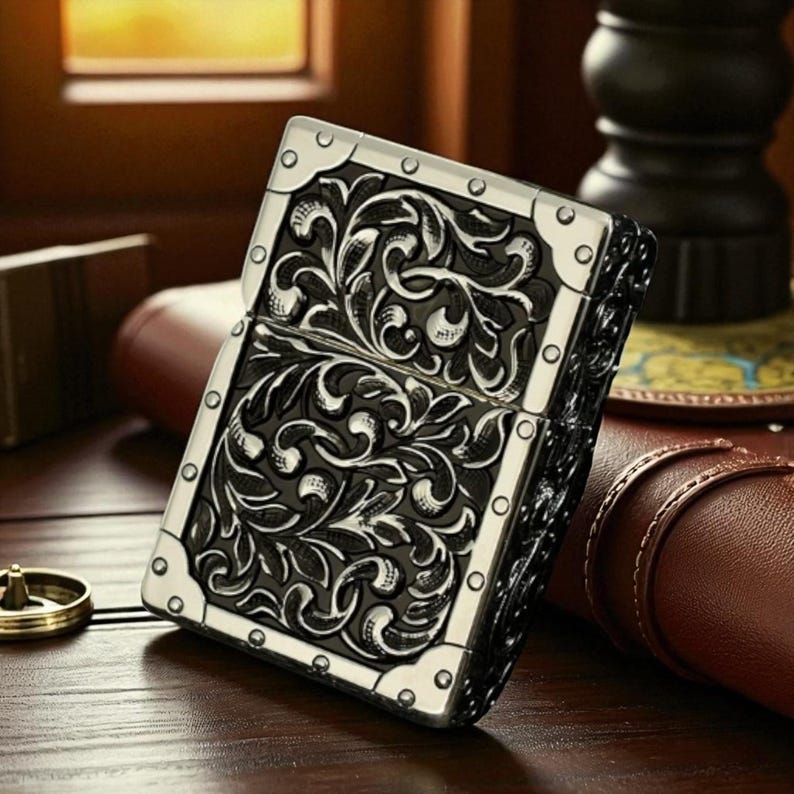 Peut inclure: Un briquet en m&eacute;tal argent&eacute; et noir avec un motif floral orn&eacute;. Le briquet a une forme rectangulaire avec des coins arrondis et est accentu&eacute; d'une garniture argent&eacute;e. Le motif est grav&eacute; sur le devant et le dos du briquet.