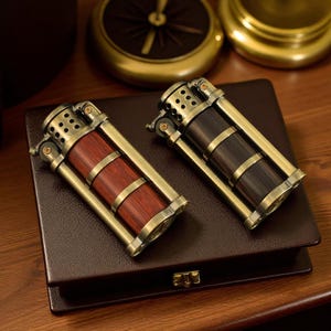 May include: Two vintage-style lighters with brass-colored frames and wooden barrels. One lighter has a reddish-brown barrel, and the other has a dark brown barrel. They rest on a brown leather box with a gold-colored clasp. The lighters have a classic, antique aesthetic.