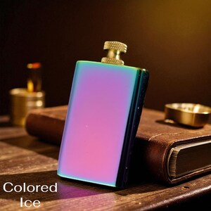 Puede incluir: Una petaca rectangular con un acabado iridiscente, que cambia de morado a verde azulado. Tiene una tapa de color lat&oacute;n y el texto "Colored Ice" en la parte inferior. La petaca est&aacute; sobre una superficie de madera con un libro encuadernado en cuero.