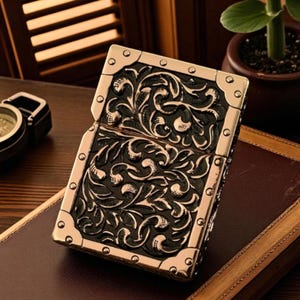 Peut inclure: Un briquet de style vintage avec un motif floral orn&eacute;. Le briquet pr&eacute;sente un fond noir avec un cadre en m&eacute;tal dor&eacute; et des coins d&eacute;coratifs. Un accessoire classique.