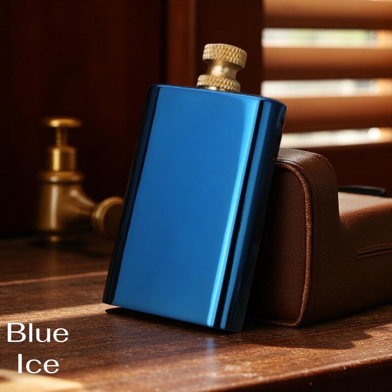 Puede incluir: Una petaca rectangular azul con una tapa dorada. La petaca tiene una superficie brillante y reflectante y las palabras "Blue Ice" est&aacute;n impresas en la parte inferior. La petaca est&aacute; sobre una superficie de madera.