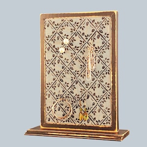 Puede incluir: Un expositor de joyas de madera con un fondo estampado en marr&oacute;n y negro. El expositor tiene un peque&ntilde;o estante en la parte inferior y cuenta con ganchos y un peque&ntilde;o estante para exhibir pendientes, collares y pulseras.