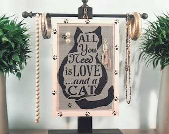 May include: A black cat silhouette jewelry organizer with the text "All you need is love...and a cat" on a white background. The organizer has a black metal stand and a black metal rod for hanging necklaces.