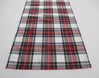 May include: A rectangular plaid table runner in a classic pattern. The design features a white background with a grid of red, black, and yellow lines. The runner is made of fabric and is designed to be placed on a table.