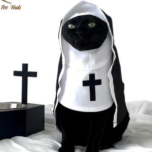 以下が含まれることがあります： 黒い猫が修道女の衣装を着ており、白いベールと胸に黒い十字架が付いています。背景には黒い十字架と黒いペットボウルがあります。「MR Print Tee Hub」のロゴが見えます。