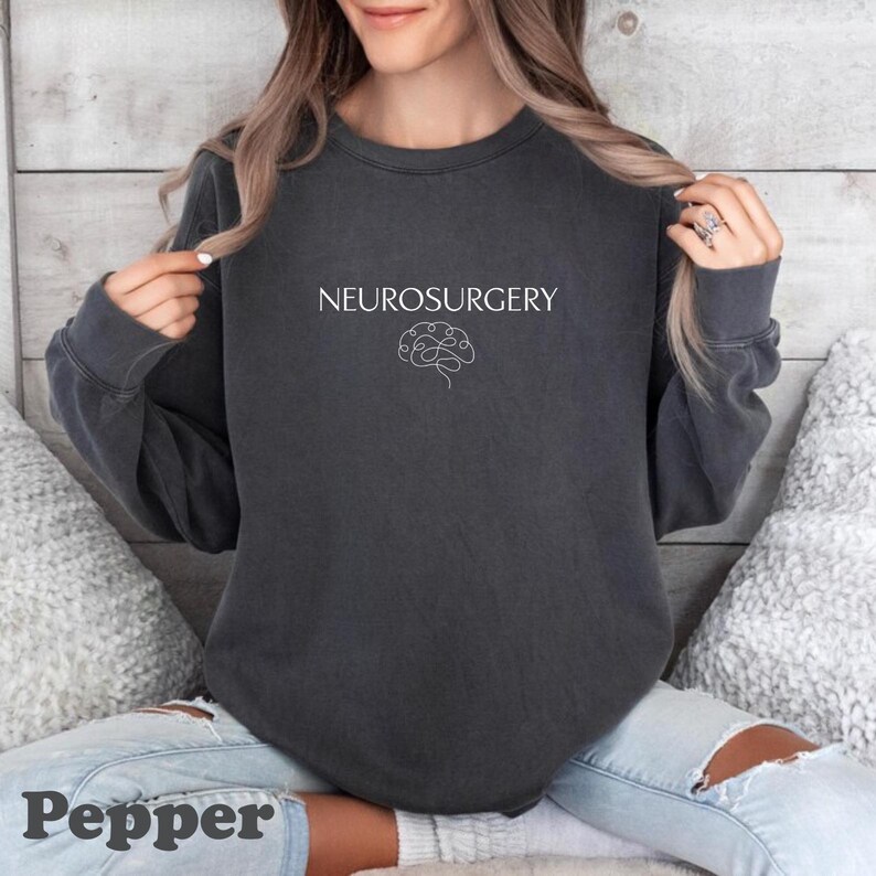 May include: A dark gray sweatshirt with the word "NEUROSURGERY" in white, above a white line drawing of a brain. The word "Pepper" is at the bottom of the image.