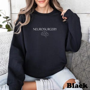 May include: Black sweatshirt with the word "NEUROSURGERY" in white, above a white line drawing of a brain. The word "Black" is printed in white at the bottom right corner of the sweatshirt.