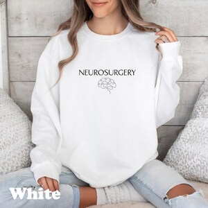 May include: White sweatshirt with the word "NEUROSURGERY" in black, above a line drawing of a brain. The word "White" is printed in a bold, sans-serif font at the bottom of the sweatshirt.