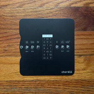May include: A black, rounded-corner card with musical chord notes and the word "chordii" printed on it. The card has musical notes and chord symbols, including C#, D, E, F#, G#, A, and B. The text "chord notes" is at the top.