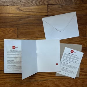 Könnte beinhalten: Eine offene, leere, bespielbare Karte mit weißem Innenraum, zusammen mit einem weißen Umschlag und einer kleinen Anweisungskarte. Die Karte hat ein rotes Kreissymbol und den Text "Blank Recordable Card". Die Artikel liegen auf einer Holzoberfläche.