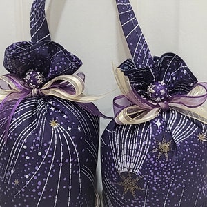 May include: Two purple fabric pouches with gold and white shooting stars and a scattering of white dots. Each pouch has a gold and purple ribbon tied around the top with a small gold and purple beaded embellishment.