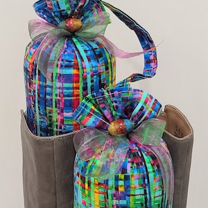 May include: Two colorful fabric shoe trees with a plaid pattern and a pink and green ribbon bow. The shoe trees are in a gray boot.