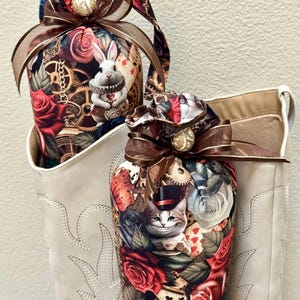 May include: Two decorative fabric pouches featuring Alice in Wonderland characters and floral designs. The pouches are adorned with brown ribbons and gold accents, and are placed inside a white boot.