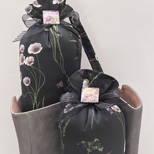 May include: Two black fabric sachets with floral patterns and iridescent square embellishments. The sachets are sitting inside a gray leather tote bag.