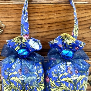 May include: Two blue fabric sachets with yellow floral patterns and blue ribbon bows. Each sachet has a blue glass bead accent.