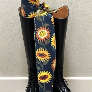 May include: A pair of black riding boots with sunflower patterned boot shapers. The shapers are made of fabric and have a navy blue background with yellow and orange sunflowers.