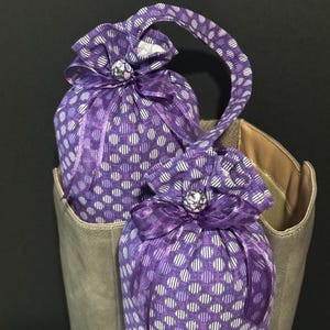 May include: Two purple and white polka dot fabric bags with a lavender ribbon and a pearl-like button. The bags are inside a brown boot.