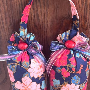 May include: Two blue fabric doorstops with a floral print in pink, red, and blue. Each doorstop has a red button and a purple and silver ribbon bow.