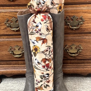 May include: Two brown fabric boot shapers with a bird and leaf pattern. The shapers are in a pair of gray knee-high boots.