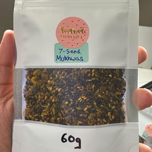 May include: A white resealable pouch with a pink and gold sticker that says "Handmade with Love". A blue sticker says "7-Seed Murkhwas". The pouch contains a mixture of brown and yellow seeds. The pouch also has a black marker label that says "60g".