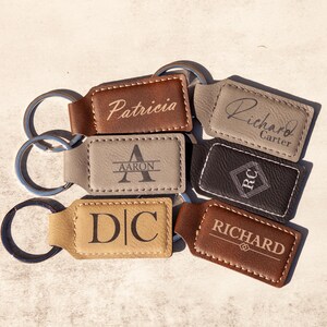 May include: A collection of six personalized leather keychains with different names and initials. The keychains are brown, tan, and gray with white stitching. The names on the keychains are Patricia, Richard Carter, Aaron, D|C, and Richard.