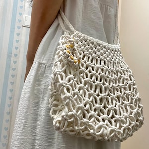May include: White crocheted tote bag with a yellow and white floral design. The bag is made of thick rope and has a wide, open top.