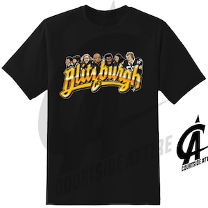 May include: Black t-shirt featuring the word "Blitzburgh" in yellow and orange script, with illustrations of football players above the text. The shirt has a crew neck and short sleeves.