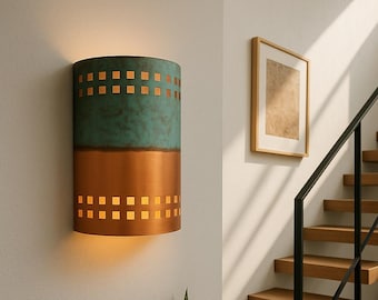 May include: A cylindrical wall sconce with a copper and teal finish. The top section is teal with a textured appearance, while the bottom is copper. Square cutouts allow light to shine through. The sconce is mounted on a white wall.