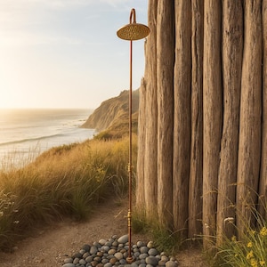 May include: Outdoor shower with a round, textured showerhead and a long, slender copper-colored pipe. The shower is set against a backdrop of a wooden wall, with a view of the ocean and a grassy hillside. The showerhead is approximately 10 inches in diameter.