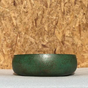 May include: A green metal bowl with a hammered finish. The bowl has a slightly rounded shape and a smooth, polished surface.