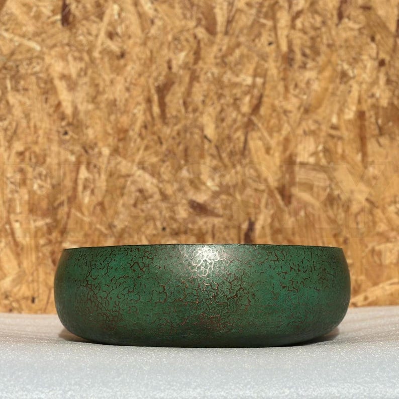May include: A green metal bowl with a hammered finish. The bowl has a slightly rounded shape and a smooth, polished surface.