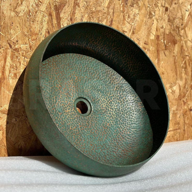 May include: A green copper hammered sink with a round shape and a drain hole in the center.