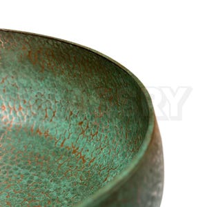 May include: Close-up of a green copper bowl with a hammered texture. The bowl has a rounded shape and a smooth, polished rim.