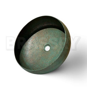 May include: A round, green copper sink with a hammered texture. The sink has a small drain hole in the center.