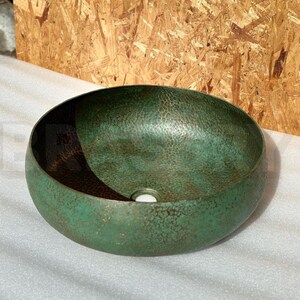 May include: A green hammered copper vessel sink with a drain hole in the center. The sink has a distressed finish and a slightly rounded shape.