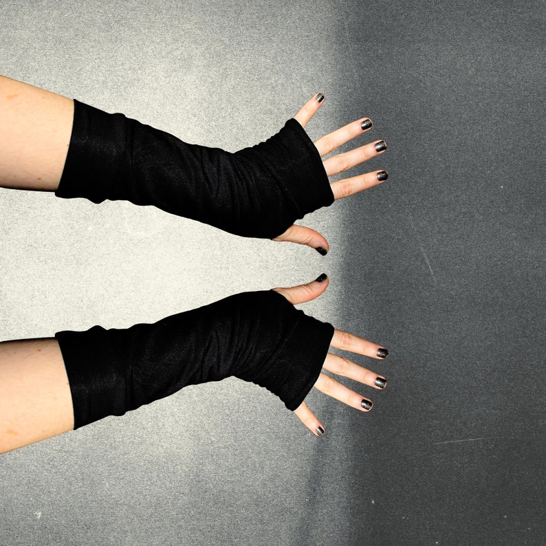 K&ouml;nnte beinhalten: Ein Paar schwarze fingerlose Handschuhe mit gerippter Textur. Die Handschuhe werden an den H&auml;nden einer Person gezeigt.
