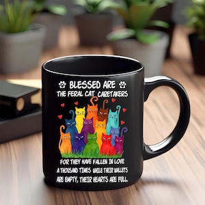 May include: Black ceramic mug featuring a colorful illustration of various cats. The mug has the text "BLESSED ARE THE FERAL CAT CARETAKERS" and a quote about love and empty wallets. A perfect gift for cat lovers.