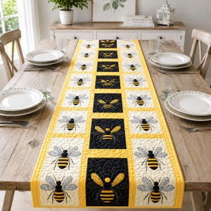 Puede incluir: Camino de mesa acolchado amarillo y negro con abejas bordadas. El camino de mesa tiene un patrón repetido de abejas sobre un fondo crema, con cuadrados negros y amarillos. Se muestra sobre una mesa de madera.