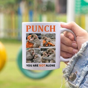 May include: White ceramic mug with the word "PUNCH" in orange block letters. The mug features four images of monkeys hugging each other and a stuffed animal. The text "YOU ARE NOT ALONE" is printed below the images.