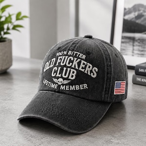 May include: A dark grey baseball cap with the text "100% Bitter Old Fuckers Club Lifetime Member" in white. The cap has a small American flag patch on the side.