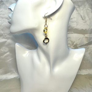 Puede incluir: Pendientes colgantes dorados con una serie de formas circulares y ovaladas conectadas. Los pendientes se muestran en una cabeza de maniquí blanca sobre un fondo suave y texturizado. Los pendientes tienen un cierre de gancho.