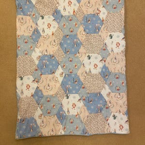 May include: A blue and pink patchwork quilt with a hexagonal pattern featuring a repeating design of Peter Rabbit characters.