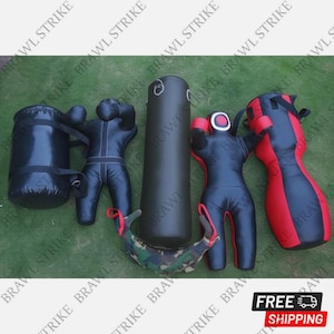 Op de afbeelding: Een assortiment zwarte en rode bokstrainingsapparatuur, waaronder een cilindrische bokszak, een druppelvormige tas en verschillende mensvormige dummies. De apparatuur is op een groene ondergrond geplaatst. De tekst "FREE SHIPPING" is zichtbaar.