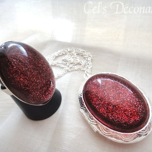 May include: A silver ring and a silver locket necklace with red glitter resin insets. The jewellery is on a white fabric background.